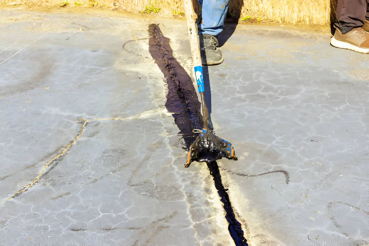 A person pushing crack sealant over a crack in pavement.