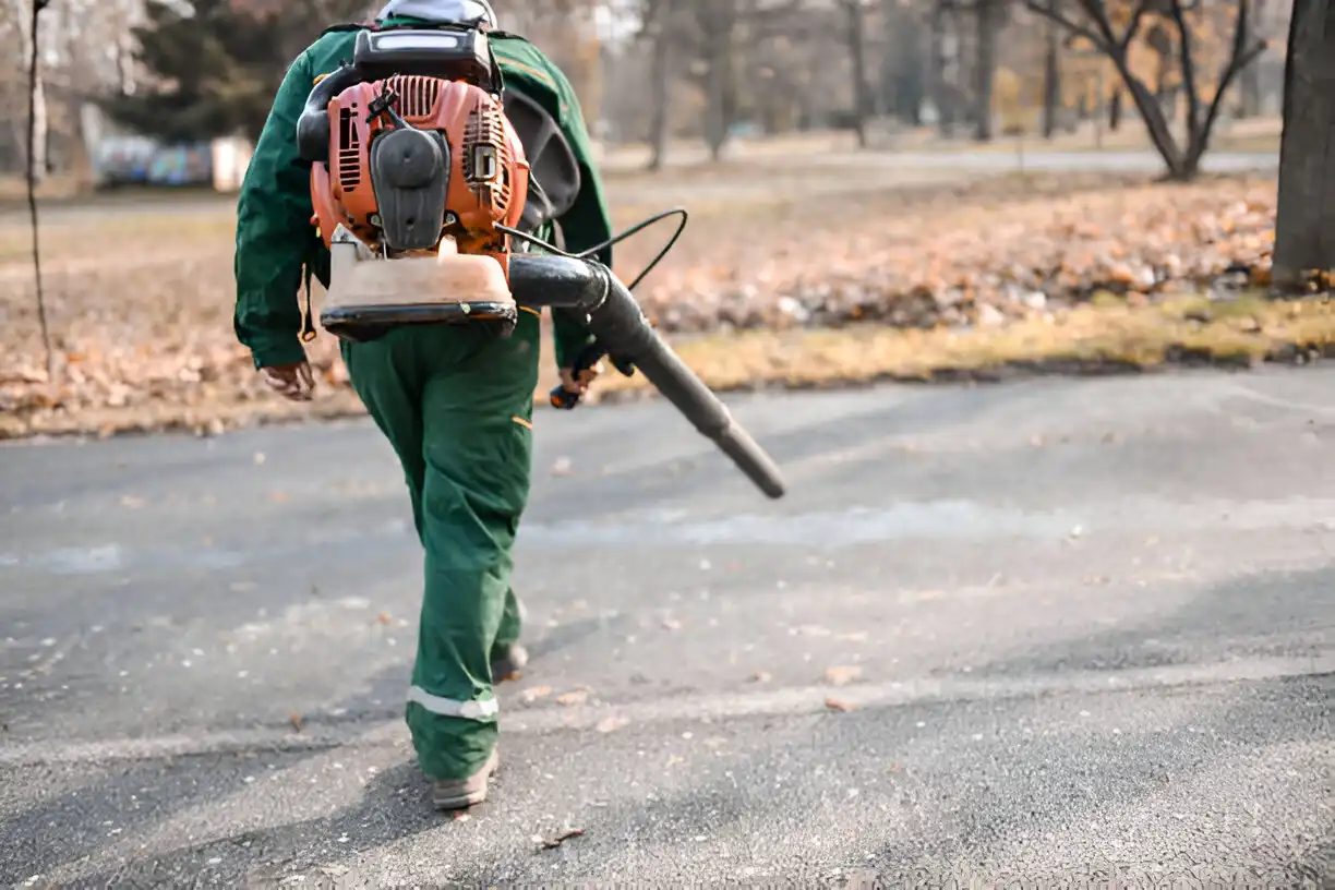 A male worker blowing off a parking lot with a leaf blower.